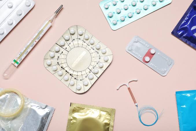 Contraceptive pill packs, an emergency contraceptive pill, a copper IUD and condoms laid out on a pink background